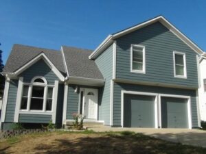 A grand house featuring an expansive driveway, set against a backdrop of trees and a sunny sky.