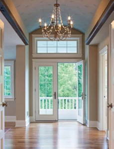 A hallway featuring an elegant chandelier and a closed door at the end, illuminated by soft lighting.