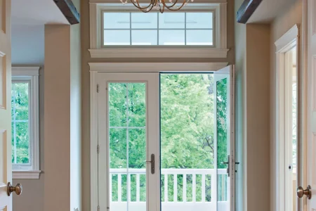 A hallway featuring an elegant chandelier and a closed door at the end, illuminated by soft lighting.